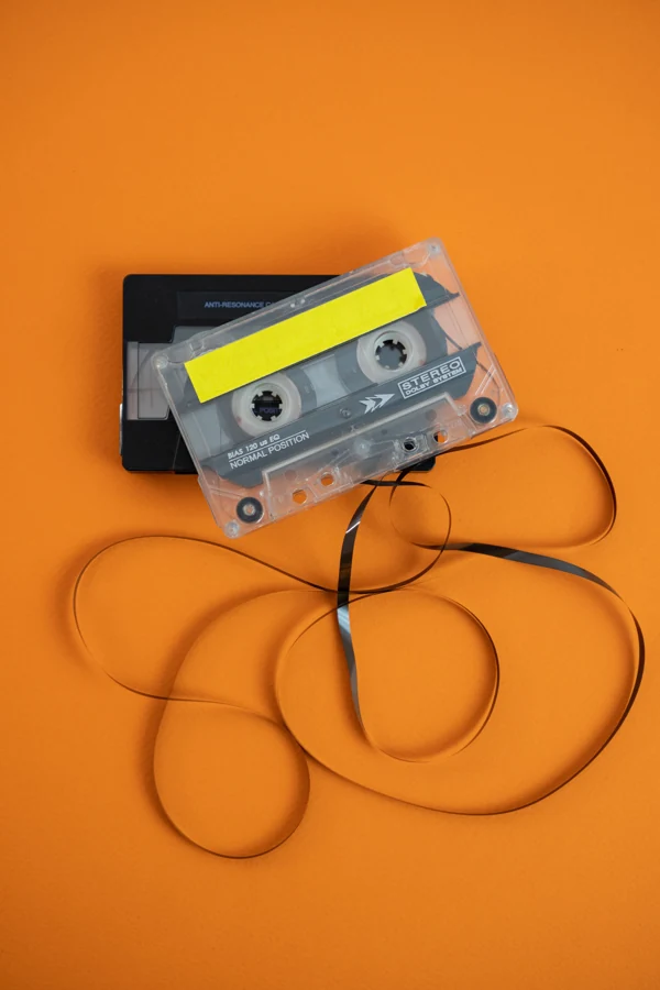 Two cassette tapes and loose ribbon on an orange background